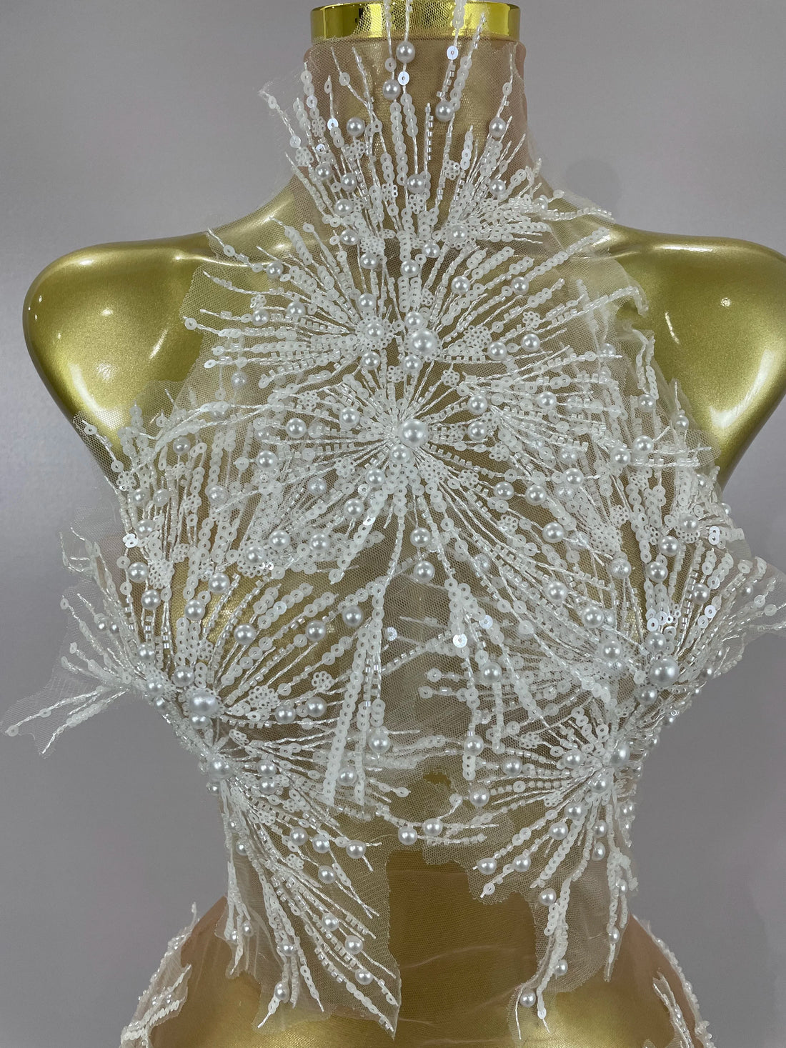 Decorative lace dress with beadwork on a gold mannequin