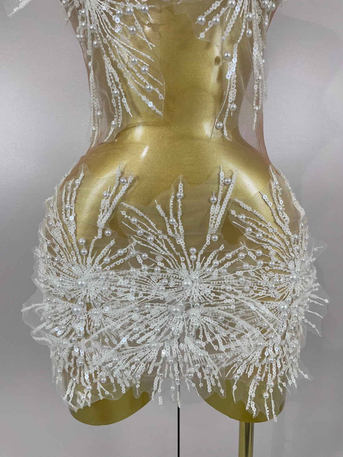 Gold dress form with intricate white floral embellishments on a plain background
