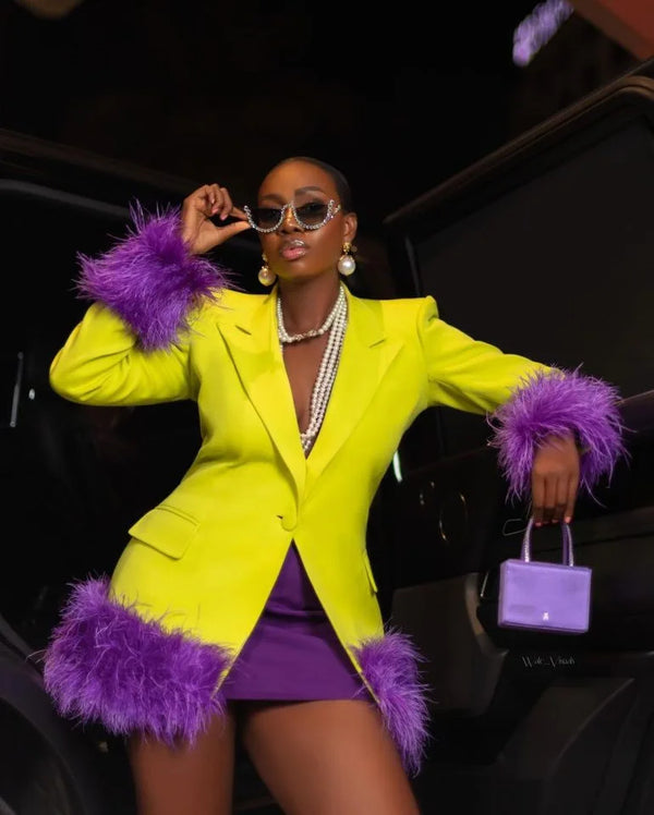 Woman in a bright yellow blazer with purple accents and a matching skirt, sitting inside a vehicle.