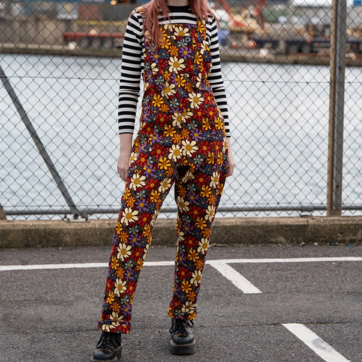 Person wearing a colorful floral jumpsuit with a striped shirt underneath, standing in an urban setting.